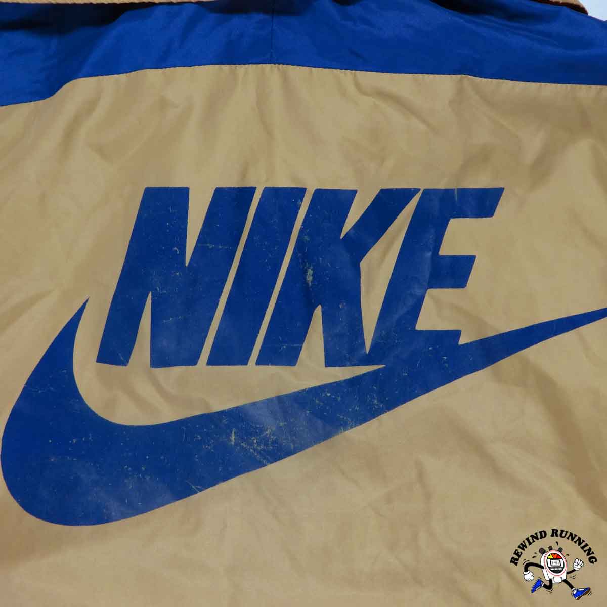 Beige vintage windbreaker jacket with a distressed blue Nike logo and brand name.